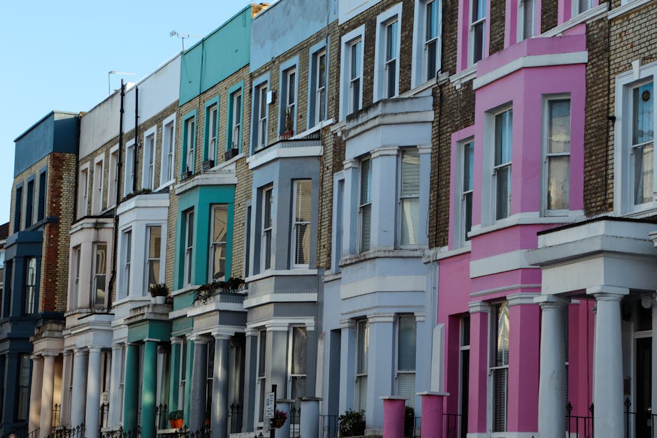 A row of Victorian terraced houses with stone facades, pitched roofs, and large sash windows along Lower Richmond Road. The buildings are surrounded by leafless trees and a well-maintained grassy area in the foreground. The scene is illuminated by soft natural daylight with a clear blue sky, reflecting the clean, exterior surfaces of the houses. The image emphasizes the historic architecture typical of Putney, showcasing the exterior of residential properties that may benefit from regular cleaning and maintenance by Putney Cleaner, as referenced on the page about clearing mould and deep cleaning in Victorian terraces.